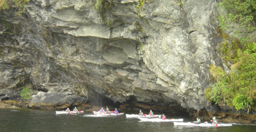 Seakayakers seeking shelter from the rain underneath a waterfall.